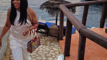 A person descending a stone staircase with a view of the sea and a thatched structure in the background.