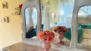A wooden dresser with a mirror, two vases with flowers, and a bed in the background. - Charming 3-bedroom house with AC and WiFi in Negril (Negril)