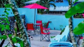 Un patio con pared azul, sillas rojas, una sombrilla roja y una fuente de agua.
