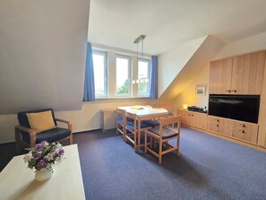 A cozy living room with a dining table, chairs, a sofa, a TV, and a window with curtains.