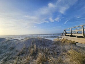 A wooden boardwalk leading to a beach with dunes and a clear sky.