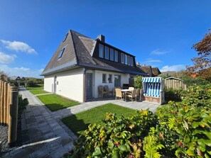 A two-story house with a sloped roof, a patio with outdoor furniture, and a garden area with plants.