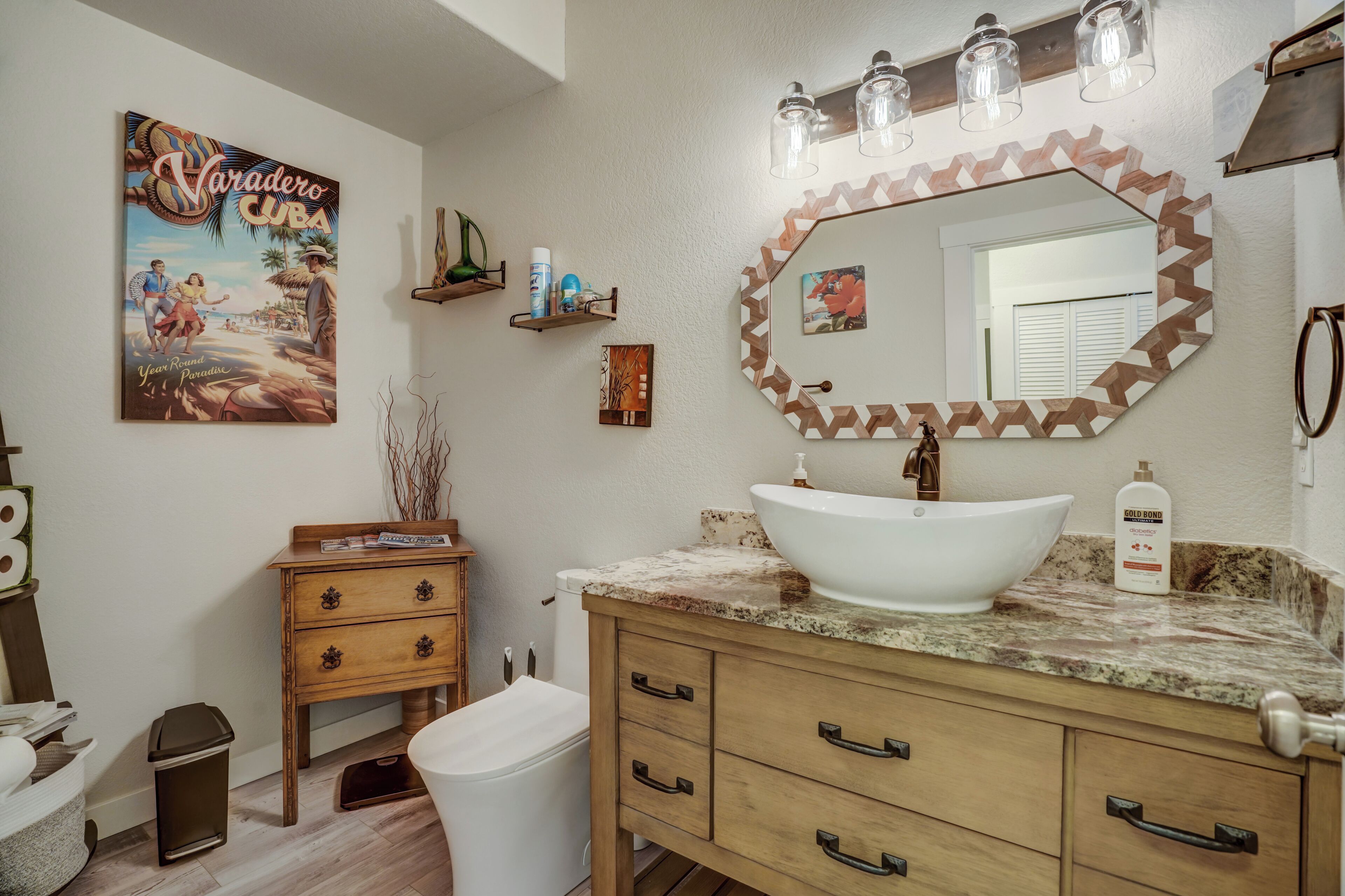 A bathroom with a large mirror, a white sink, wooden vanity, and a picture of Varadero, Cuba.