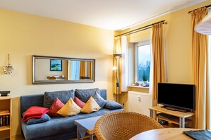 A living room with a sofa, television, and a window with curtains.