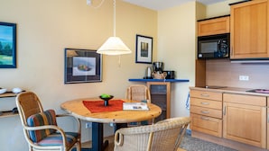 A compact kitchen with a dining area, including wicker chairs, a round table, a hanging lamp, and wooden cabinets.