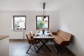 Un comedor con una mesa lista para cuatro personas, dos sillas, un banco y una lámpara colgante.