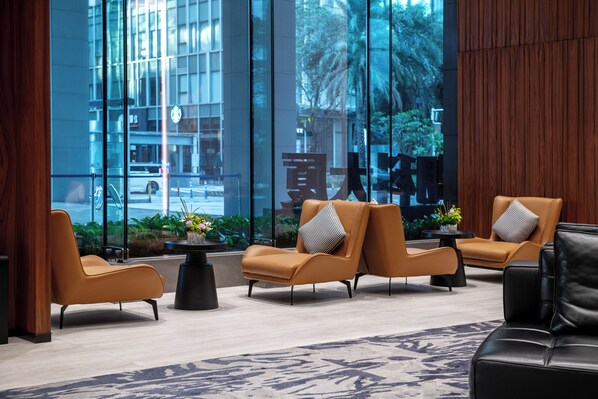 Un hall d’entrée moderne avec des fauteuils en cuir, un canapé noir et une grande fenêtre donnant sur la rue et la verdure.