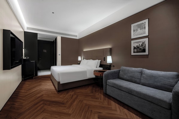 A modern hotel room with a bed, a gray sofa, a nightstand, and two framed pictures on the wall. - SHENZHENWANXIANGQINGHUAJIUDIAN (Shenzhen)