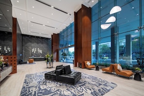 A modern lobby with a black sectional sofa, orange armchairs, and a patterned rug. - SHENZHENWANXIANGQINGHUAJIUDIAN (Shenzhen)