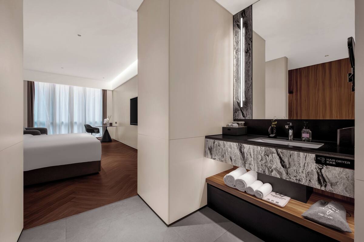 A modern hotel room with a large bed, a bathroom with a marble countertop, and a view of the city.