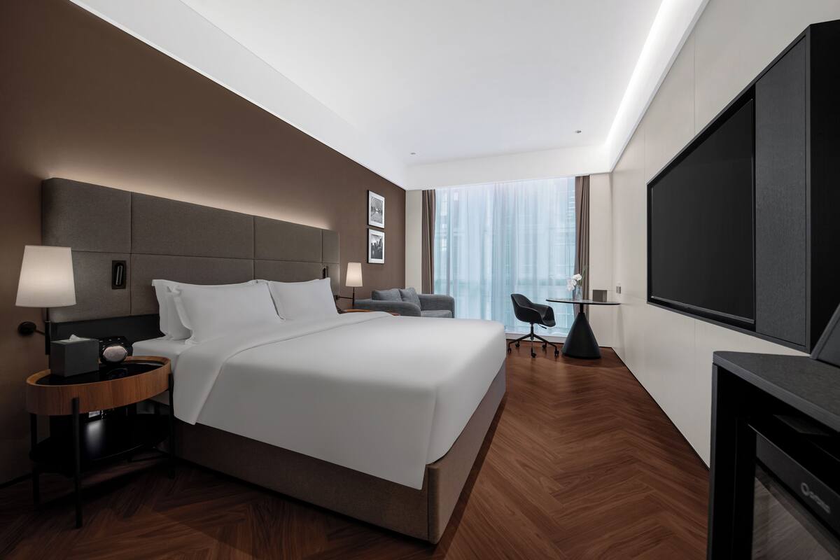 A modern hotel room with a large bed, a desk, a chair, and a TV.