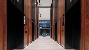 Un moderno vestíbulo de hotel con un mostrador de recepción central, paneles de madera y suelo de baldosas.