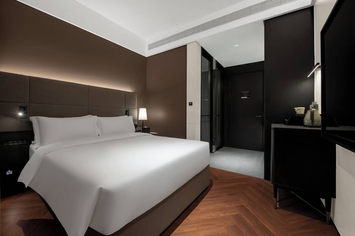A modern hotel room with a large bed, bedside tables, a desk, and a walk-in closet.