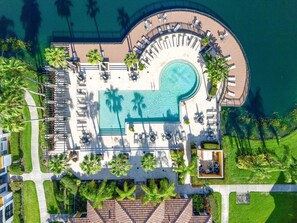 Vue aérienne d’un complexe hôtelier doté d’une grande piscine, de chaises longues et de palmiers.