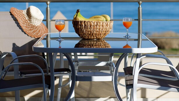 Ein Tisch mit einem gewebten Korb, zwei Orangensaftgläsern und einem Strohhut auf einem Balkon mit Meerblick.