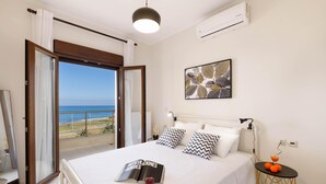 Ein Hotelzimmer mit Bett, Nachttisch, Klimaanlage an der Wand, Deckenleuchte und Fenster mit Meerblick.