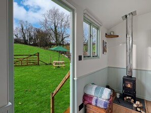 A cozy room with a wooden bench outside, a green umbrella, and a wood-burning stove inside. - Foxgloves Shepherd's Hut, Brompton Regis (Nr Dulverton)