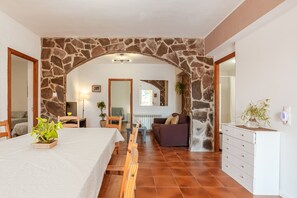 Una habitación con un arco de piedra, una cama, un sofá, un aparador y una mesa de comedor con sillas.
