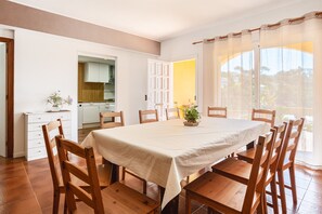 Un comedor con una mesa dispuesta para seis personas, sillas de madera, una planta en maceta y vistas a través de amplios ventanales.