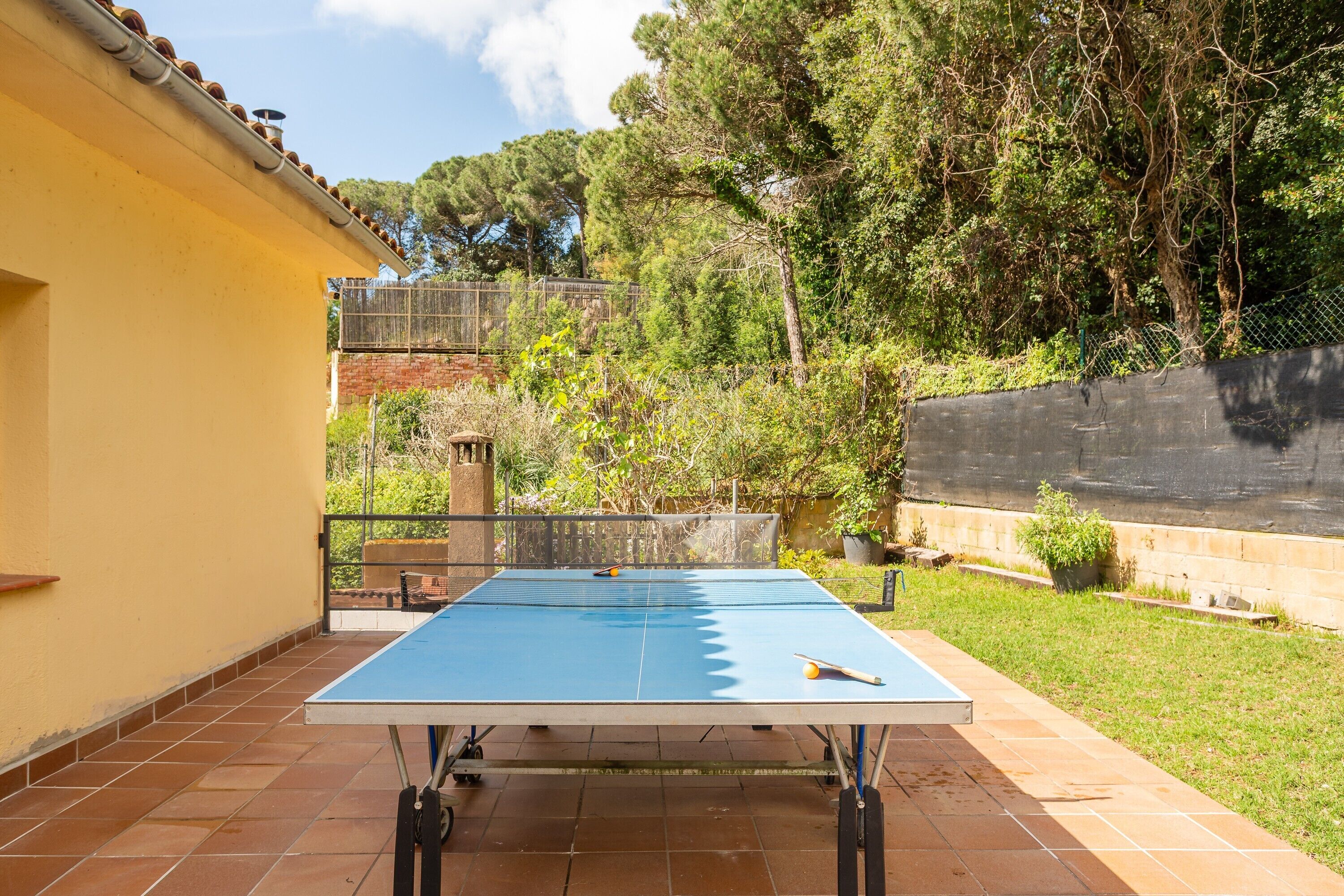 Taula de ping-pong en un pati exterior amb una paret groga i una tanca al fons.