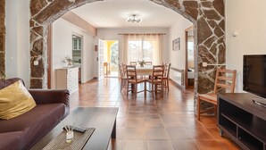 A living room with a stone archway, a dining area, a sofa, a TV, and a fireplace.