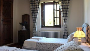 Quarto com duas camas, janela com cortinas, radiador, luminária e guarda-roupa de madeira.