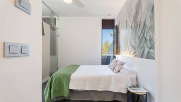 Een moderne slaapkamer met een bed, een groene plaid, een klein tafeltje en een schilderij aan de muur.
