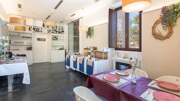 Comedor con mesas dispuestas para una comida, zona de cocina con botellas de vino y vistas al exterior.