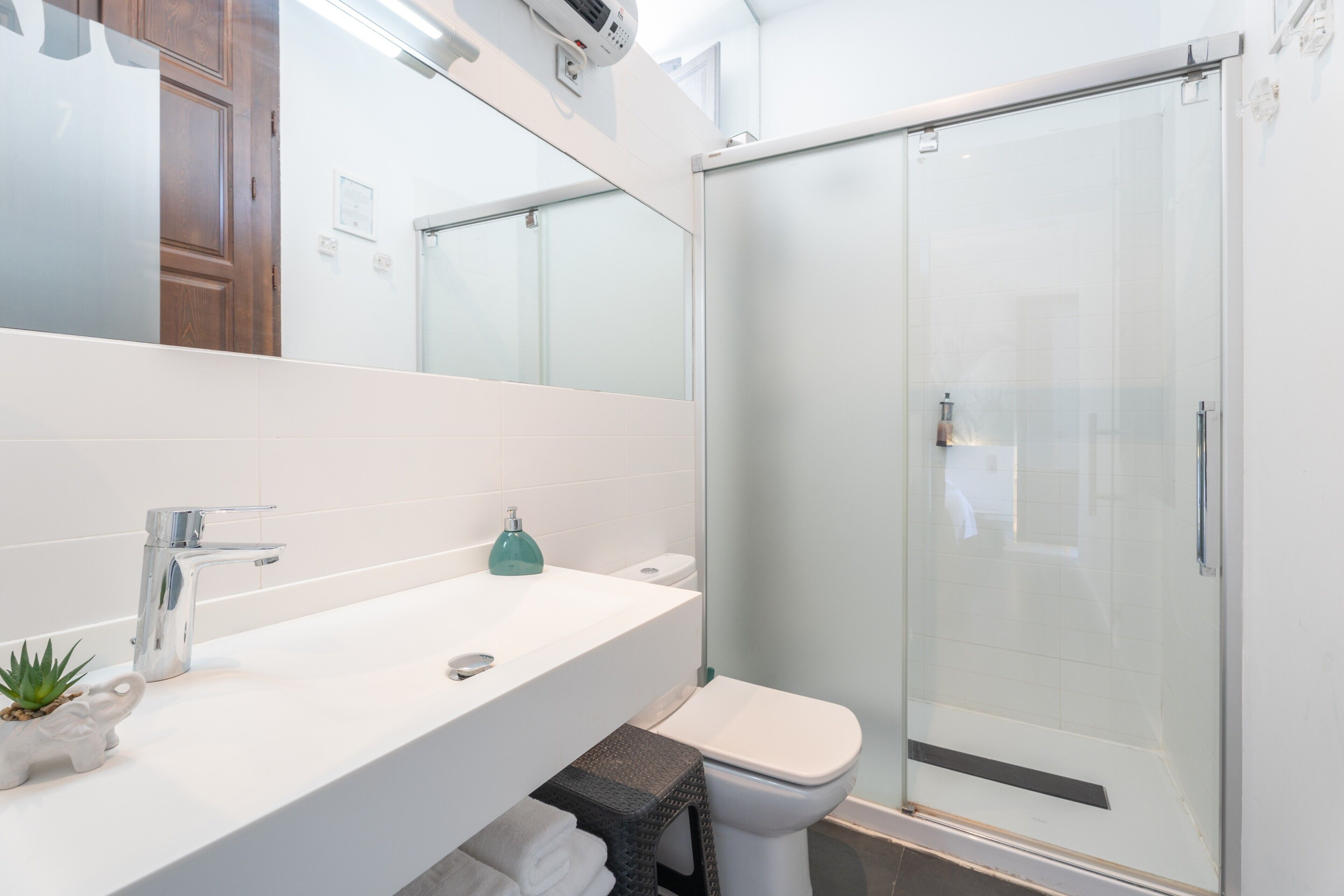 Une salle de bain moderne avec un lavabo blanc, une douche en verre et des toilettes apparentes.