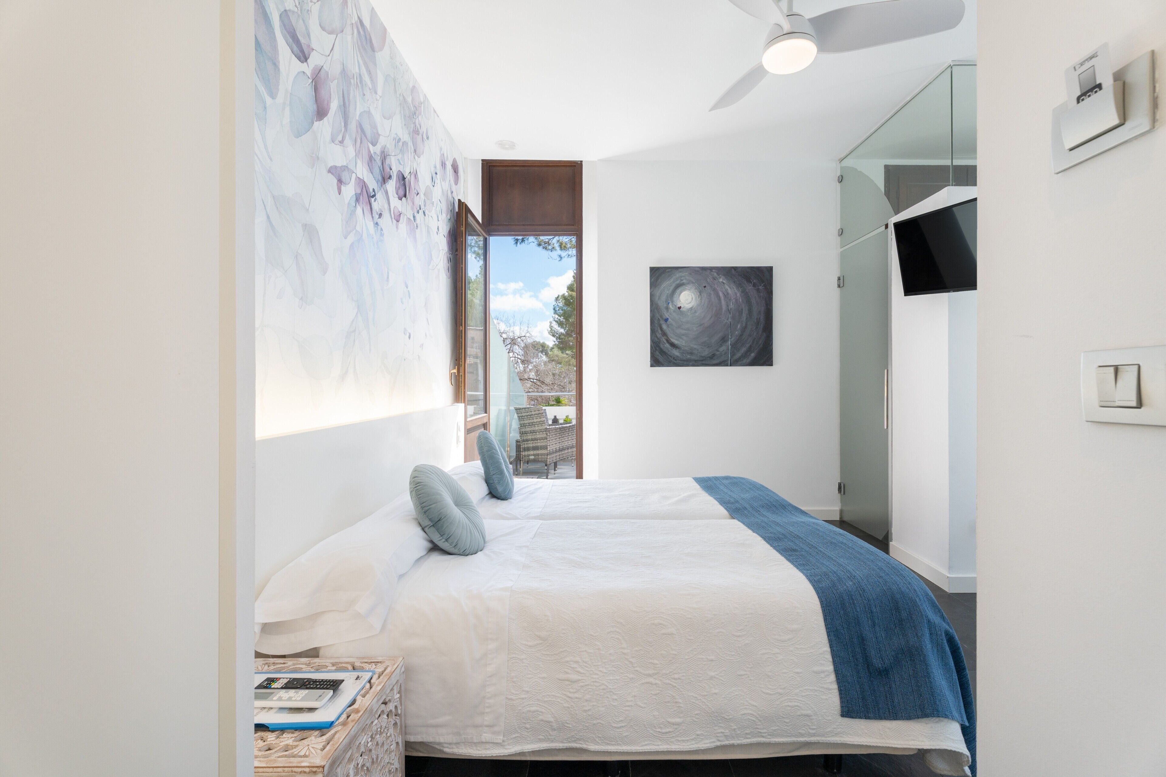 Een moderne slaapkamer met een bed, een plafondventilator, een schilderij en een raam.
