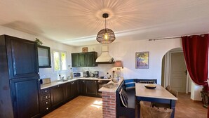 A modern kitchen with dark cabinets, a central island, and a dining area with a table and chairs. - Villa Giulia - sea view (Sant'Antonino)