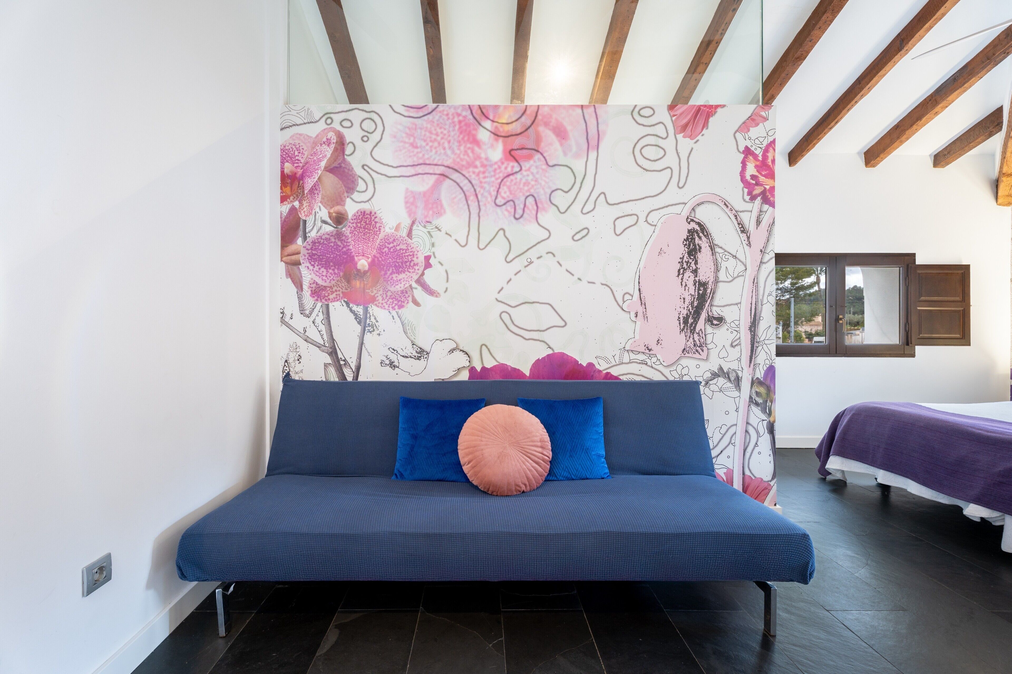 Una habitación moderna con un sofá azul, un cojín rosa y un mural floral en la pared.