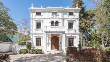 A white building with a symmetrical facade, a central entrance with a wooden door, and a small balcony above the entrance.