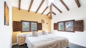 Ein Schlafzimmer mit einem großen Bett, Holzbalken an der Decke, einem Nachttisch und einem Fenster mit Fensterläden.