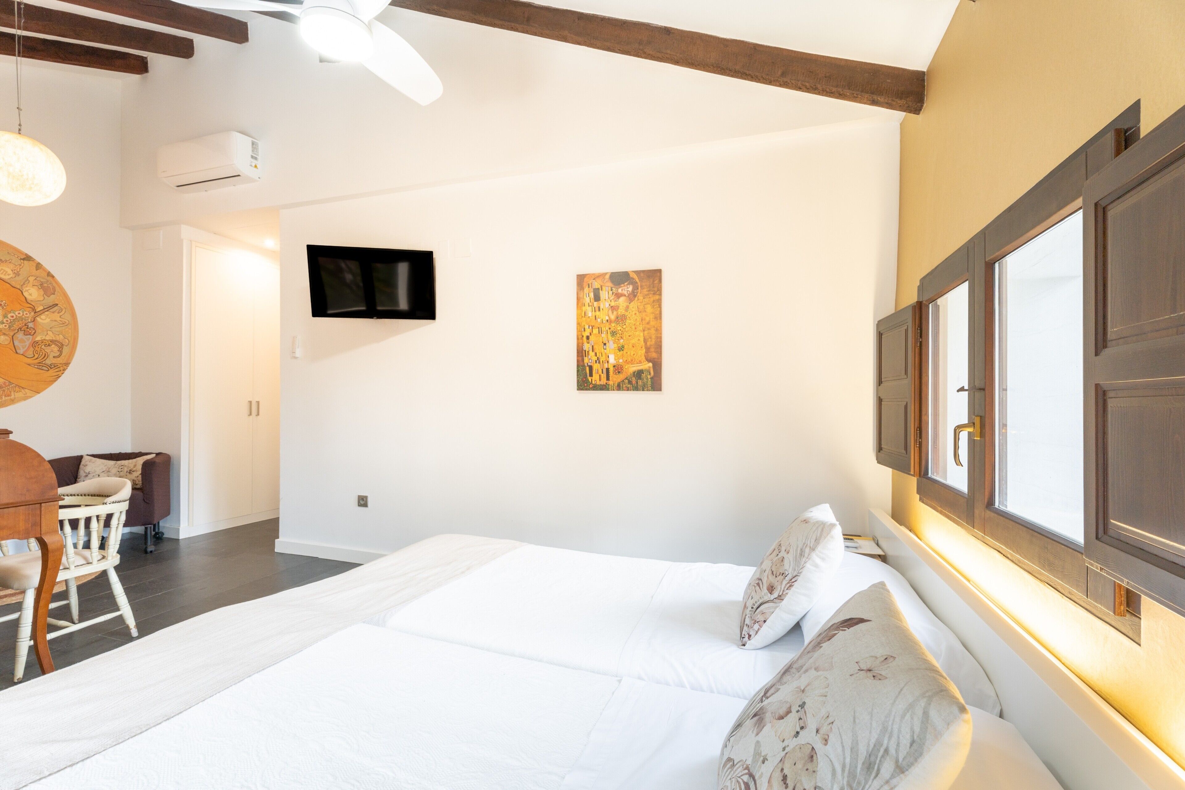 Una camera da letto con un letto grande, una televisione appesa al muro e una finestra con tende.
