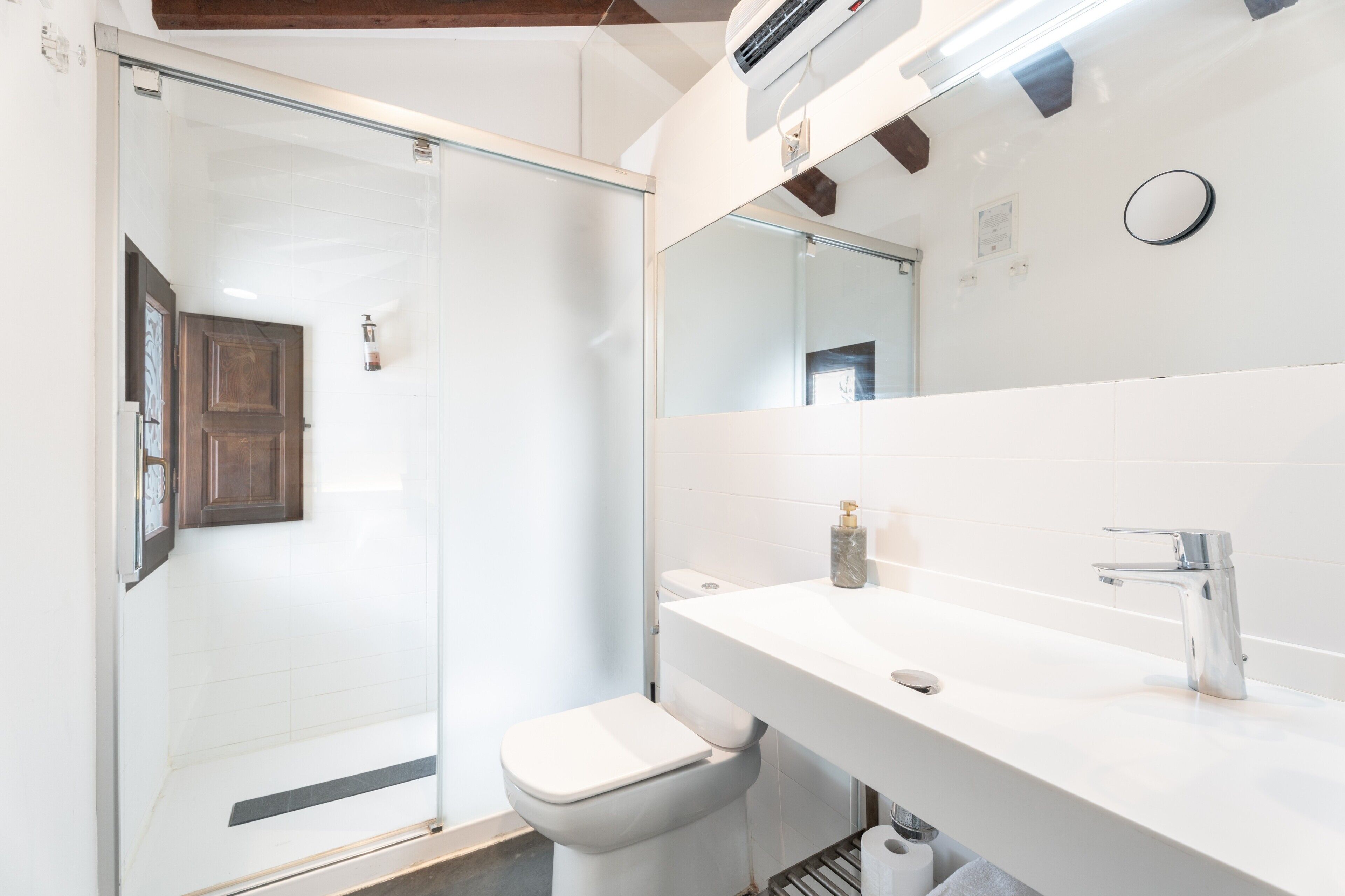 Casa de banho moderna com cabine de duche em vidro, sanita branca e lavatório branco com espelho por cima.