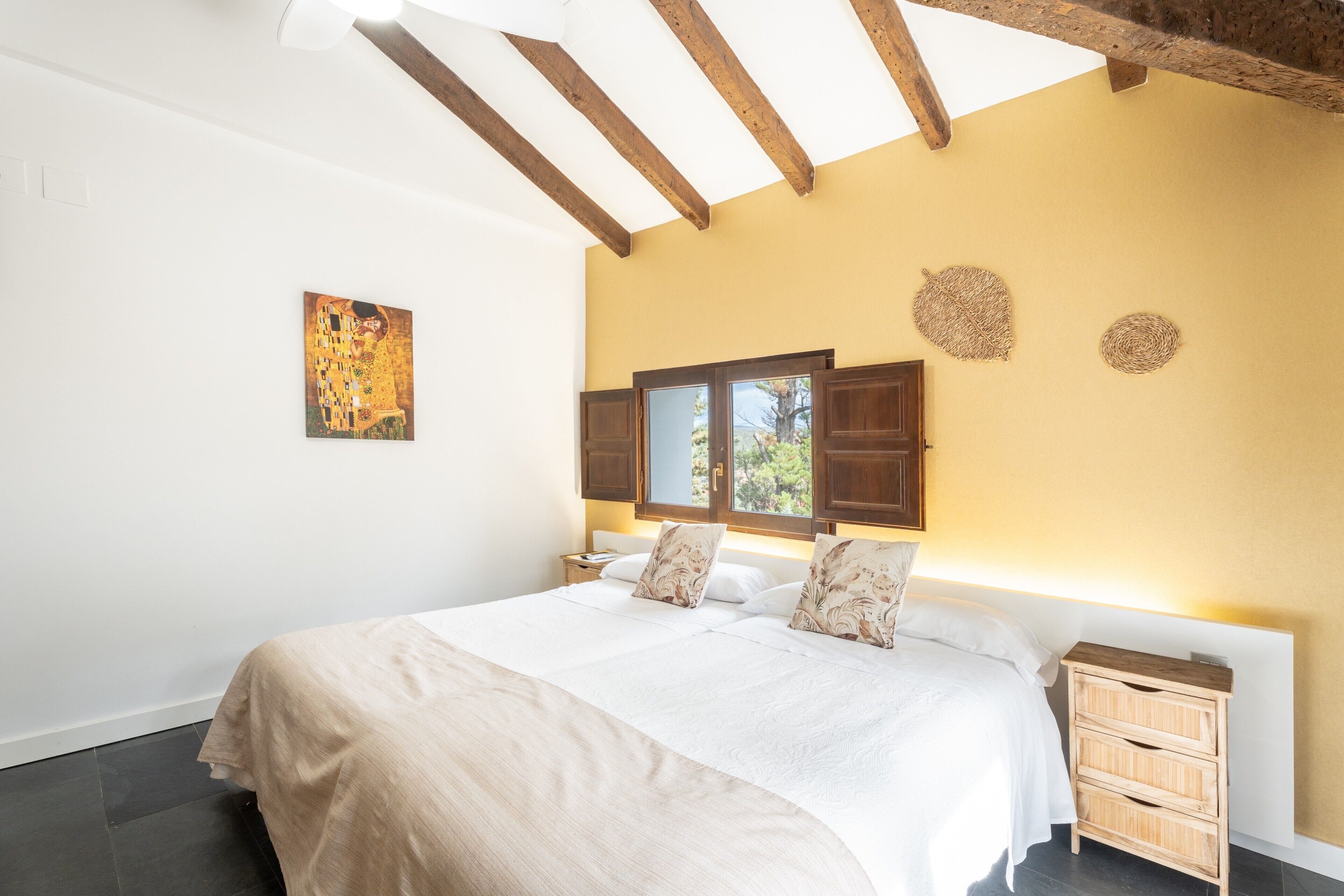 A bedroom with a bed, wooden headboard, bedside tables, and a window with shutters.