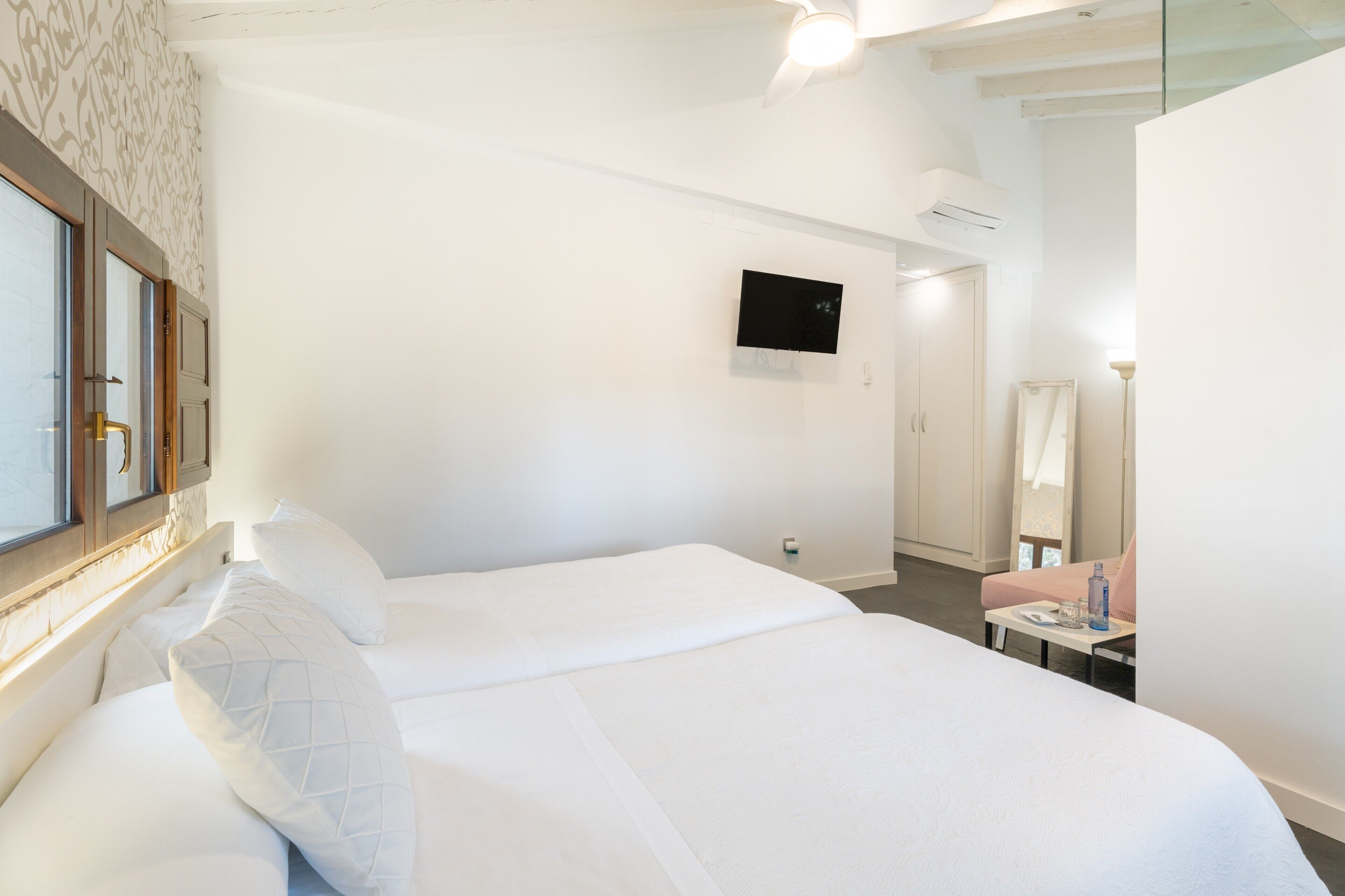 Een hotelkamer met twee bedden, een aan de muur bevestigde televisie, een spiegel en een kleine tafel met een lamp.