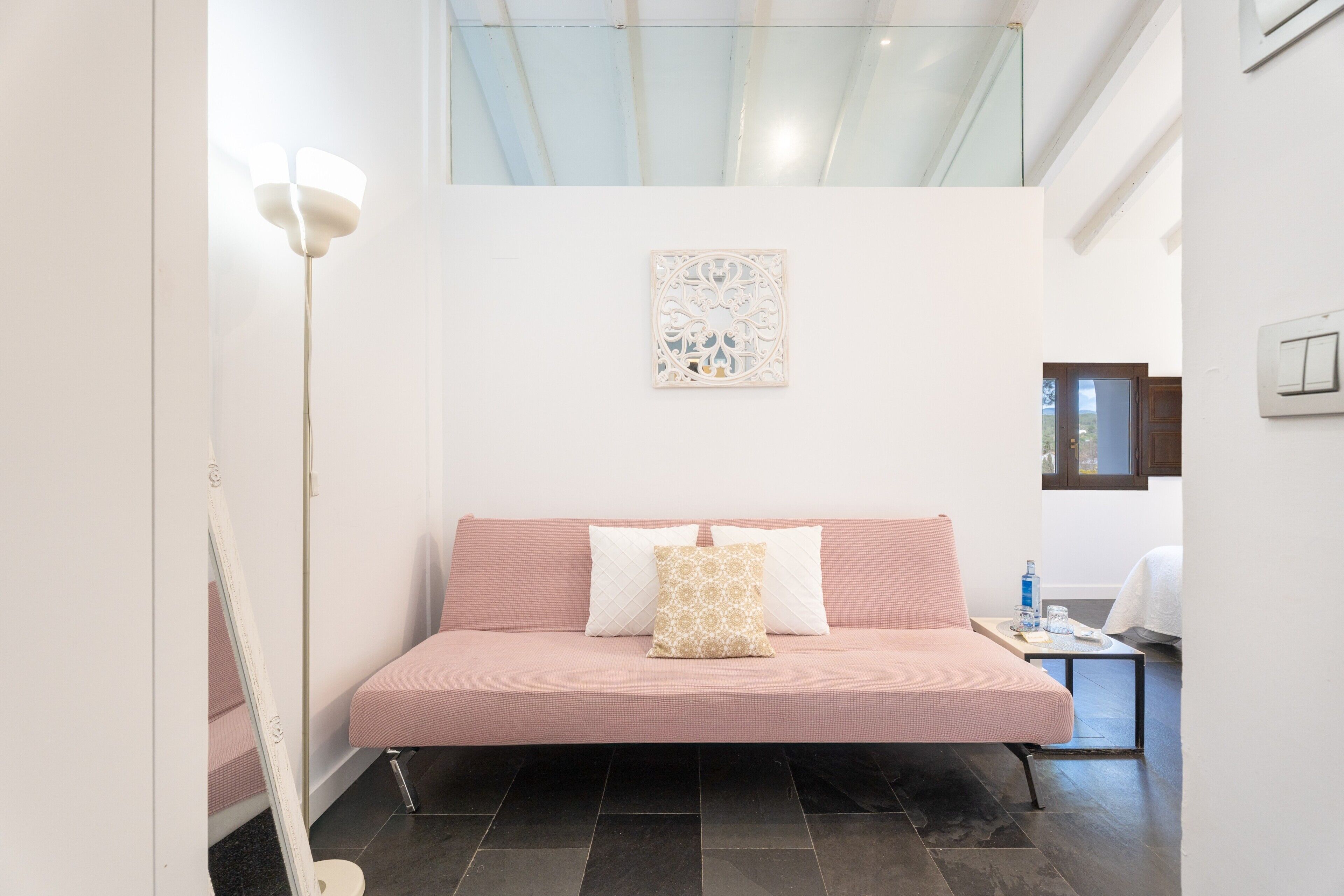 A bedroom with a bed, a bedside table, a wall-mounted light, and a window.