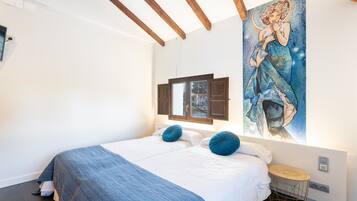 Un dormitorio con una cama, una obra de arte colgada en la pared y una pequeña mesa redonda.