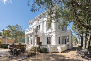 A white building with a balcony, outdoor seating, and trees.