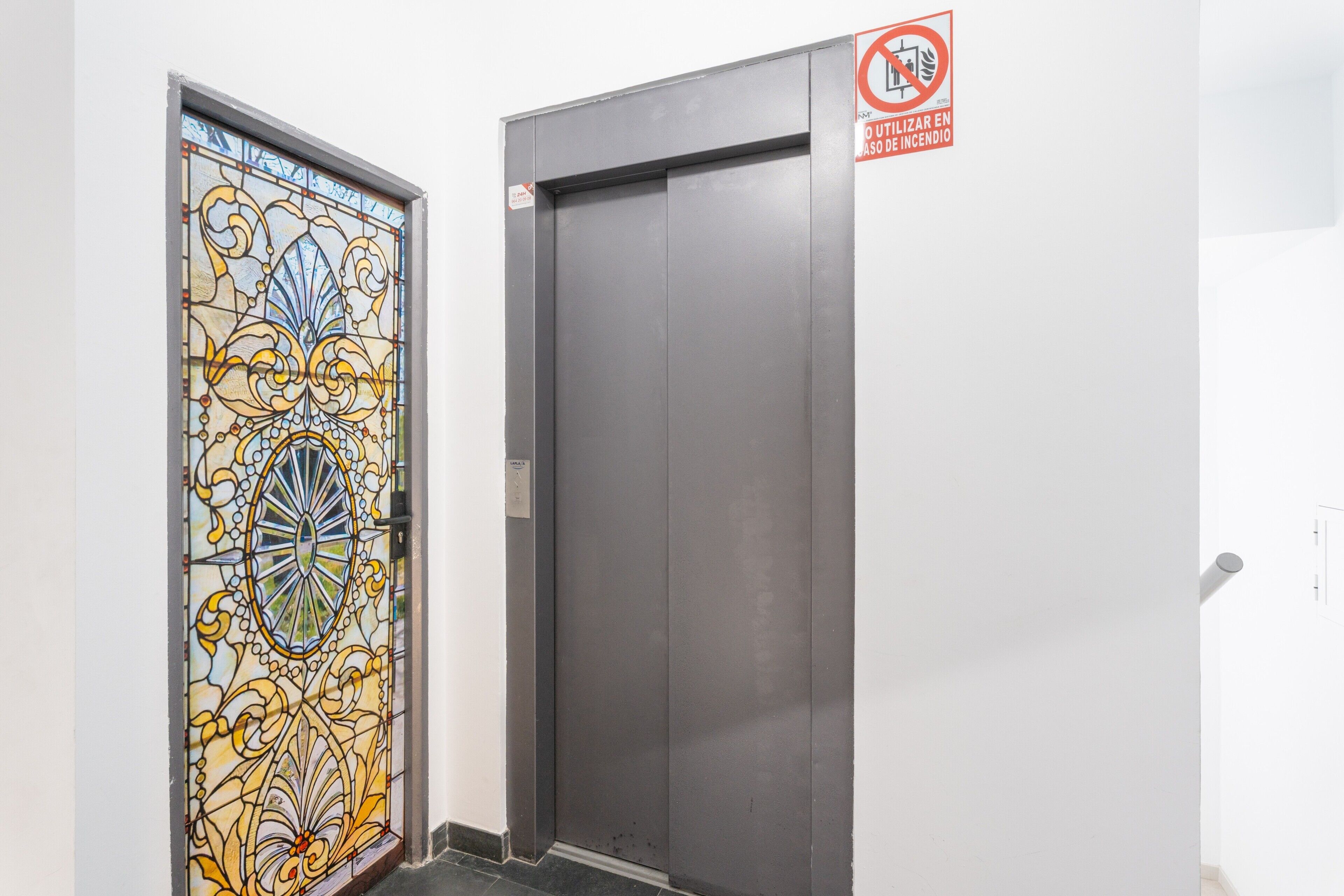 Una puerta con un diseño de vitral y una puerta de ascensor sencilla.