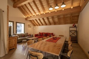 Una habitación amplia con un alto techo de madera, una larga mesa de comedor y una zona de estar acogedora con sofá y sillones.