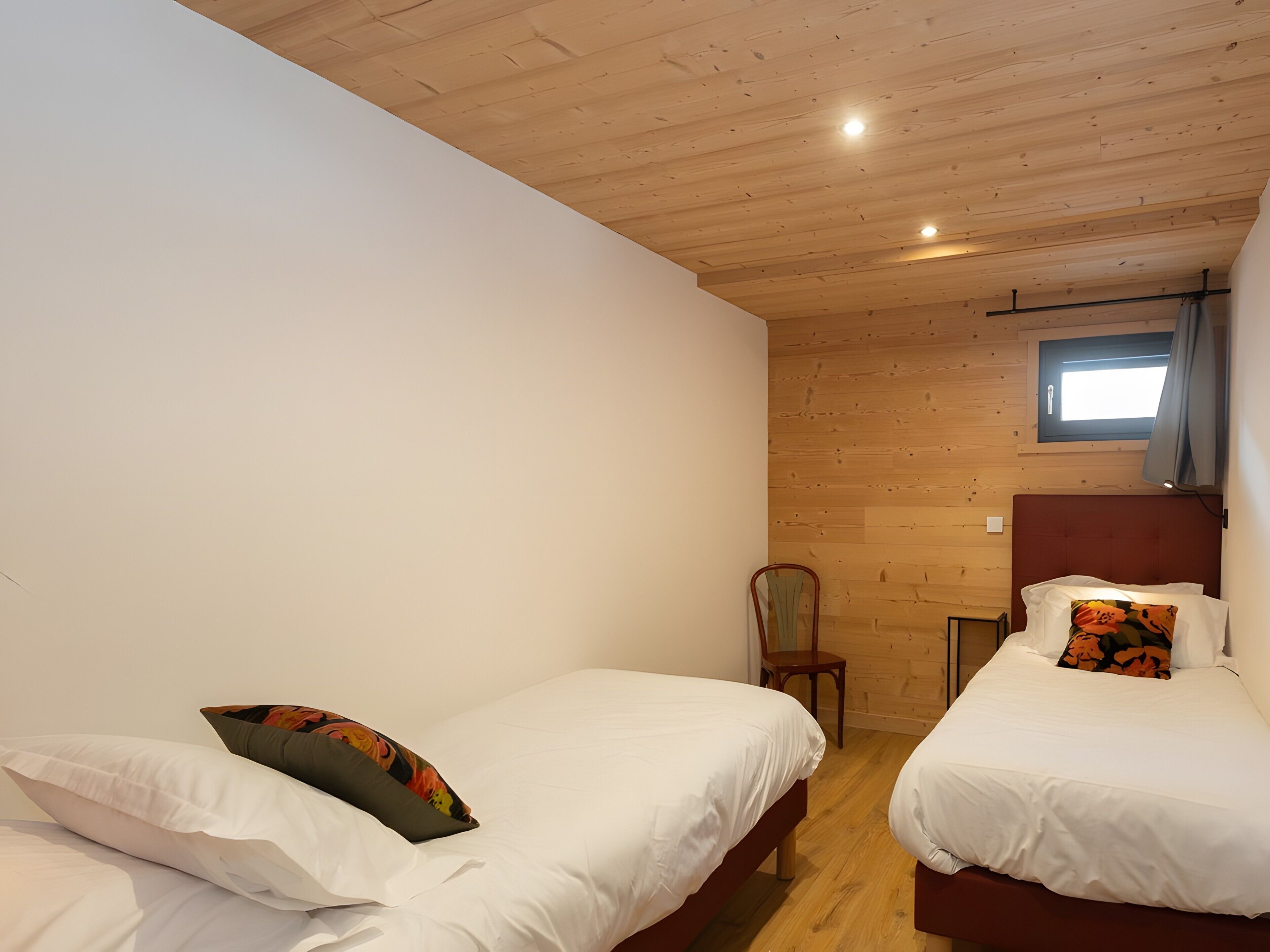 Een kamer met twee bedden, een houten plafond, een raam met gordijnen en een stoel.