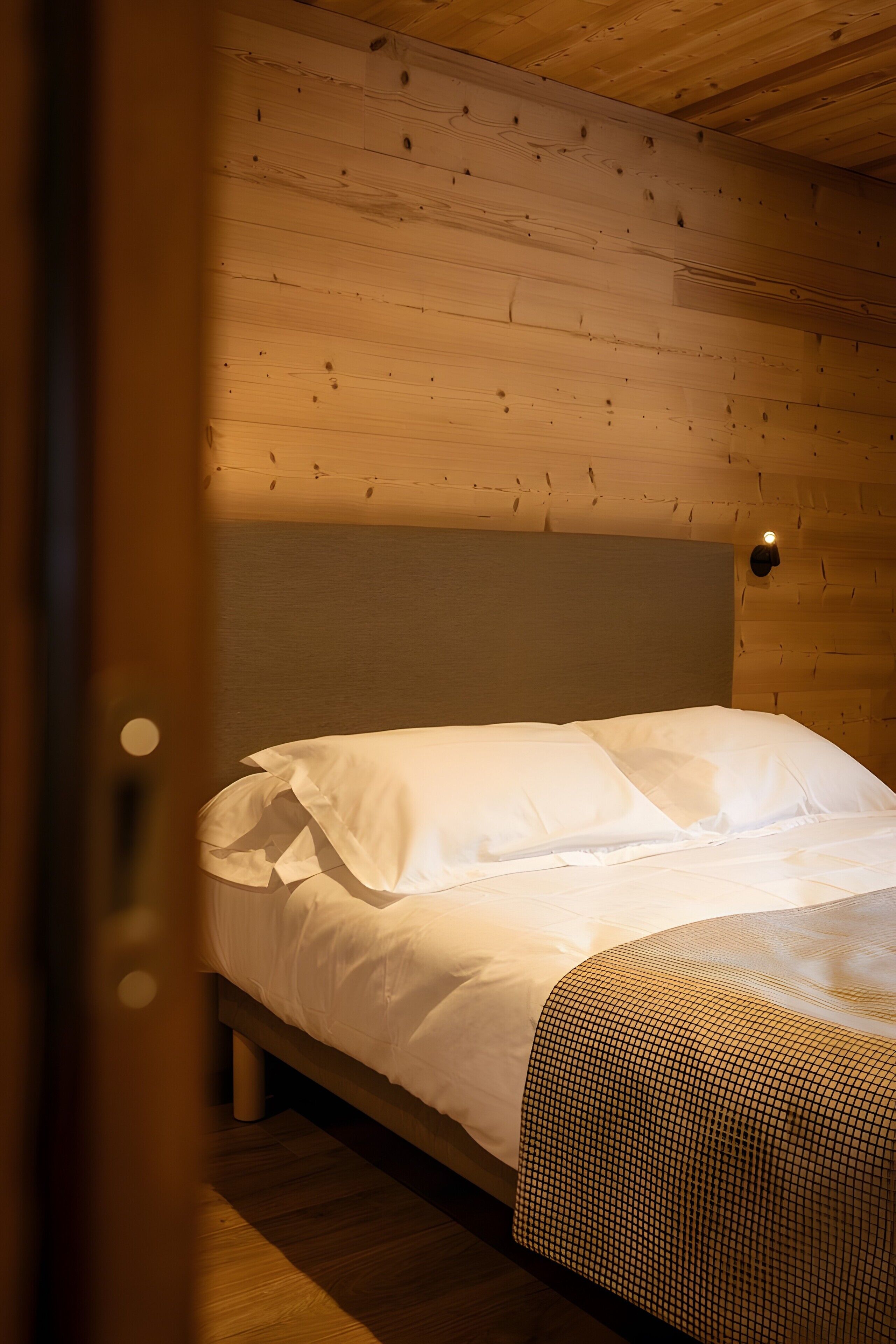 Una cama individual con ropa de cama blanca en una habitación con paredes y suelo de madera.