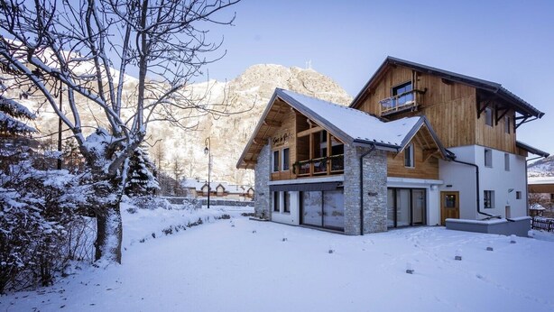 Un moderno chalet con fondamenta in pietra, livelli superiori in legno e tetto spiovente.