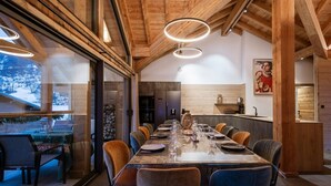 A dining area with a long table, chairs, and a view through large windows. - Chalet '-Spa Le Cervin' with Mountain View, Private Terrace and Wi-Fi (Valloire)