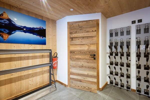 A room with a wooden ceiling, a painting of a mountain landscape, a wooden door, and a wall with black hand-shaped objects.