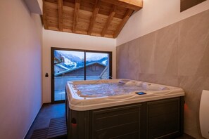 Un jacuzzi en una habitación con techo de madera y vistas a una montaña nevada.