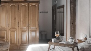 Ein Schlafzimmer mit Holzschrank, Bett mit weißer Bettdecke, Nachttisch mit Weinglas, Teekanne und Tasse.
